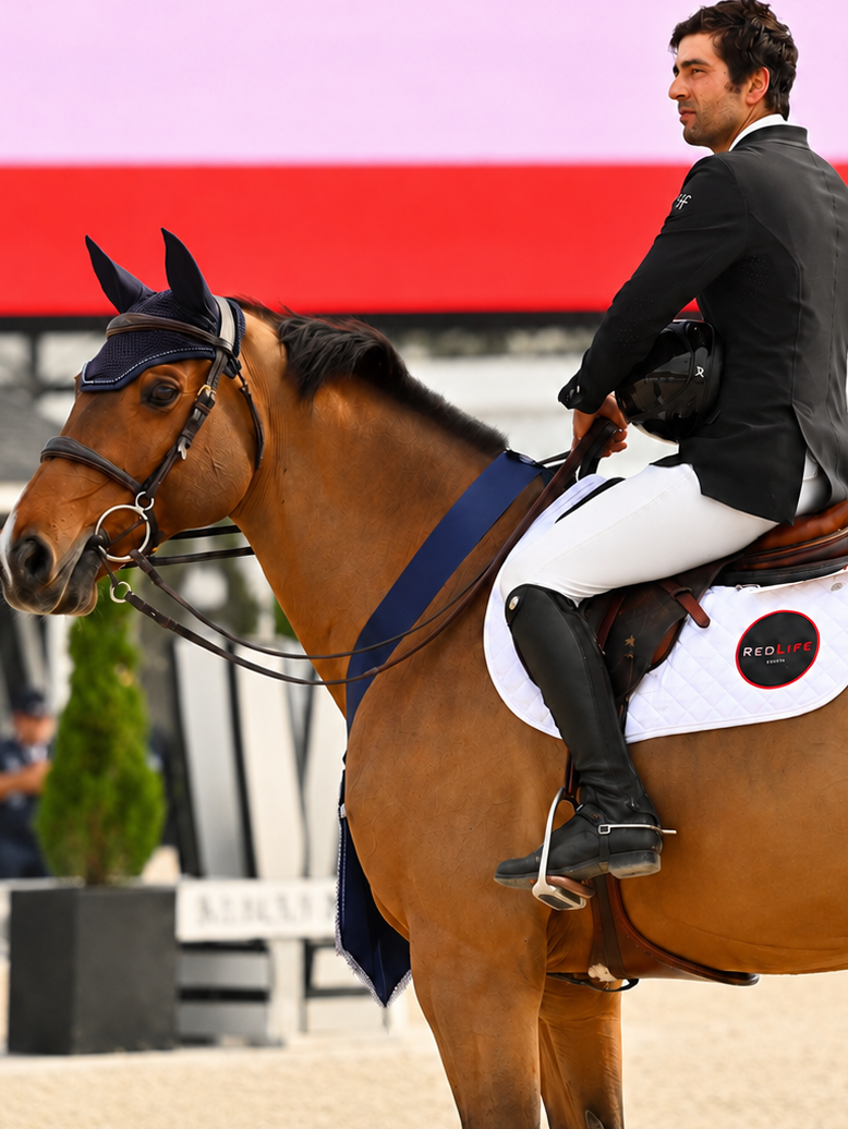 Jad Dana wins Grand Prix in International Arena wearing a RedLife saddle pad with horse wearing the winning sash for her class. 